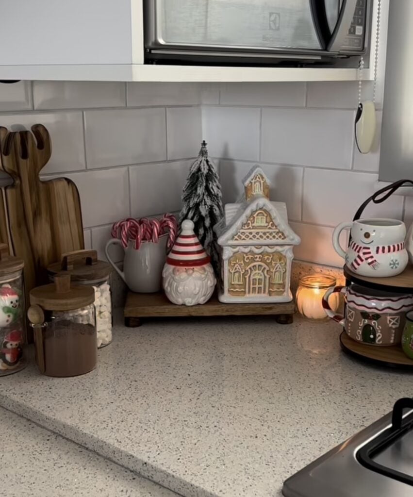 Gingerbread hot cocoa bar with snowman mugs, gingerbread houses, greenery, and layered Christmas kitchen decor, featured by slowestuff.com.