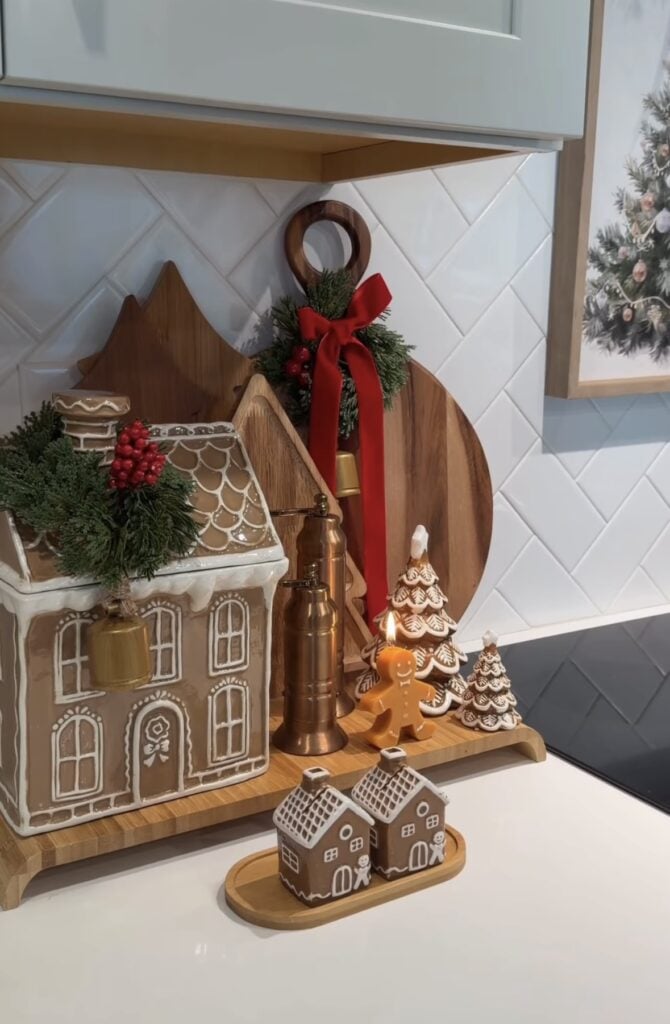 Gingerbread kitchen counter with house-shaped canister, layered cutting boards, mini Christmas trees, and salt and pepper shakers, featured by slowestuff.com.