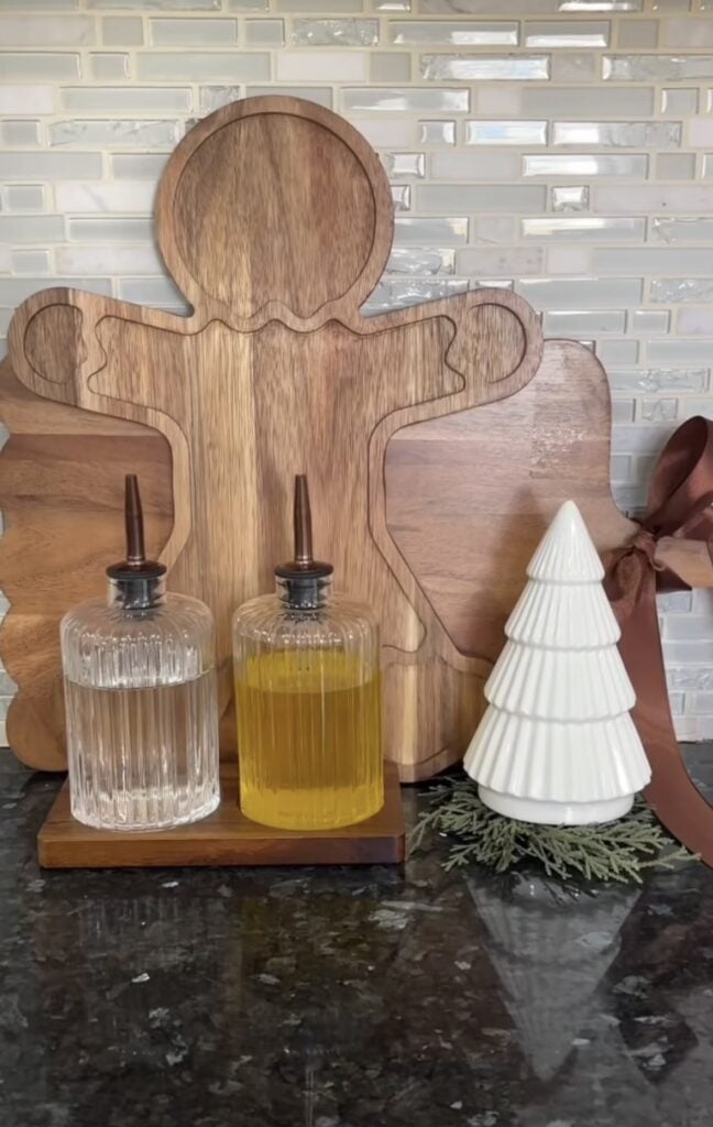 Gingerbread kitchen counter with gingerbread man cutting board, oil bottles, ceramic Christmas tree, and festive accents, featured by slowestuff.com.