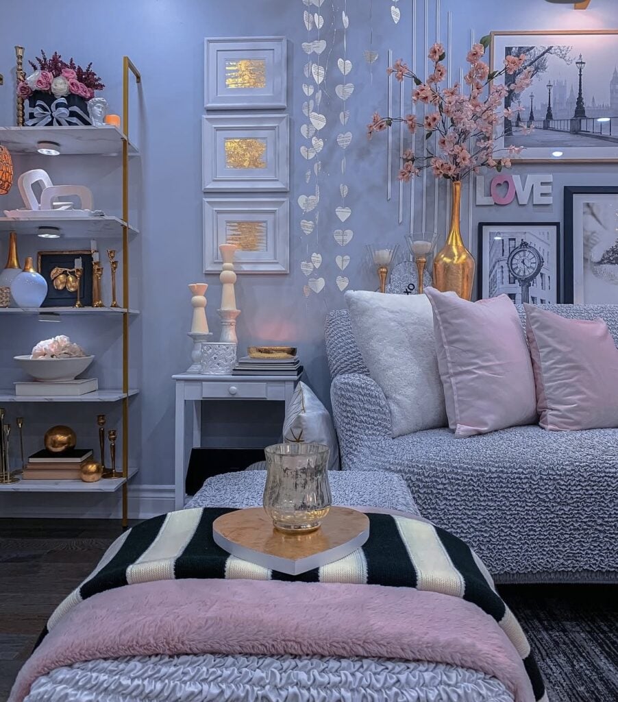 Glam Valentine’s Day living room with gray sofa, blush pillows, hanging heart garland, gold vase with pink branches, and pink accents.
