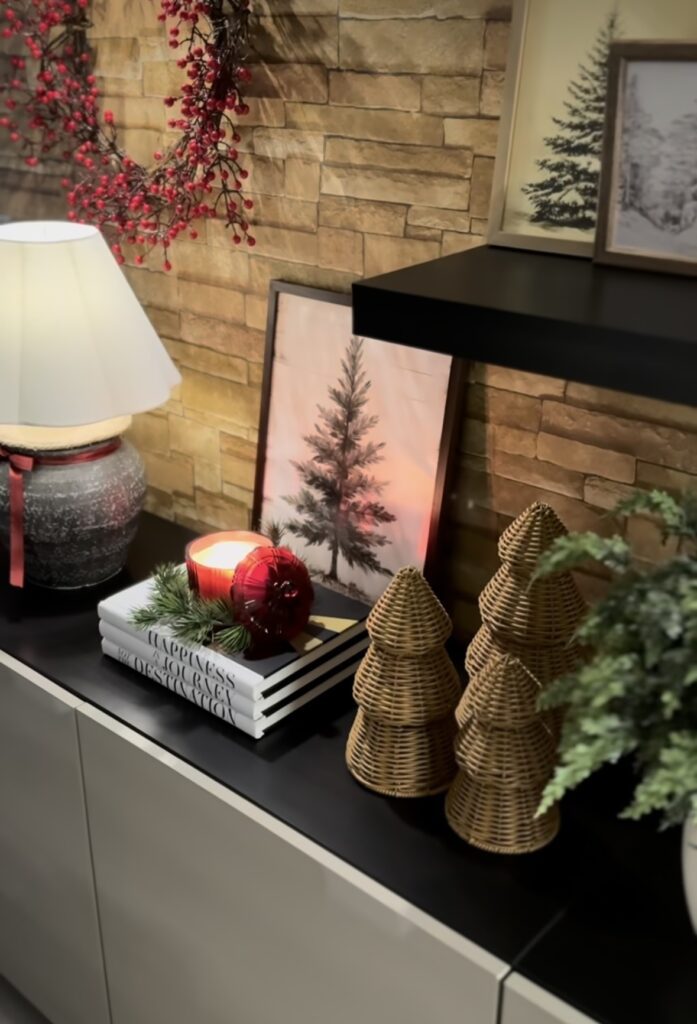 Cozy Christmas console table against a stone wall with tree artwork, a red candle, and woven Christmas trees, featured by slowestuff.com.
