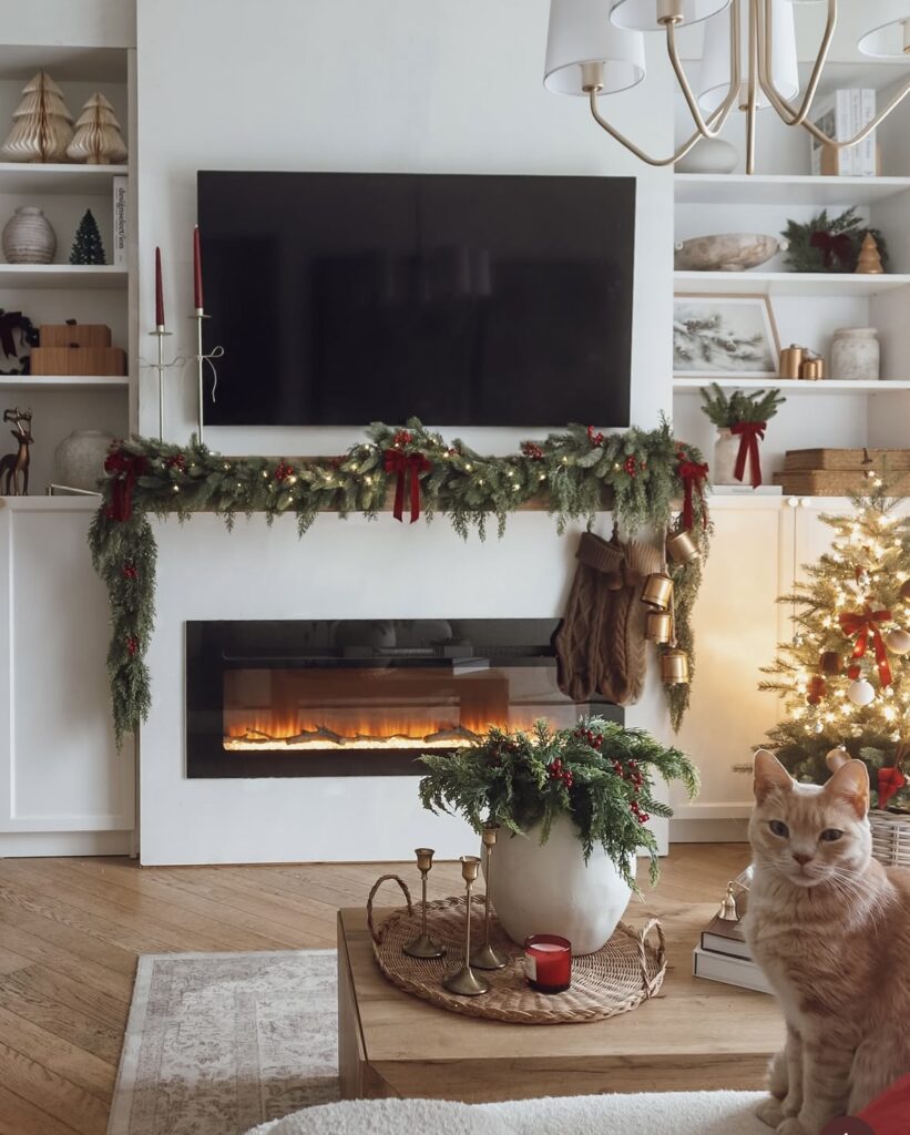Modern Christmas fireplace decorated with evergreen garland and red bows beside a festive coffee table and Christmas greenery, featured by slowestuff.com.