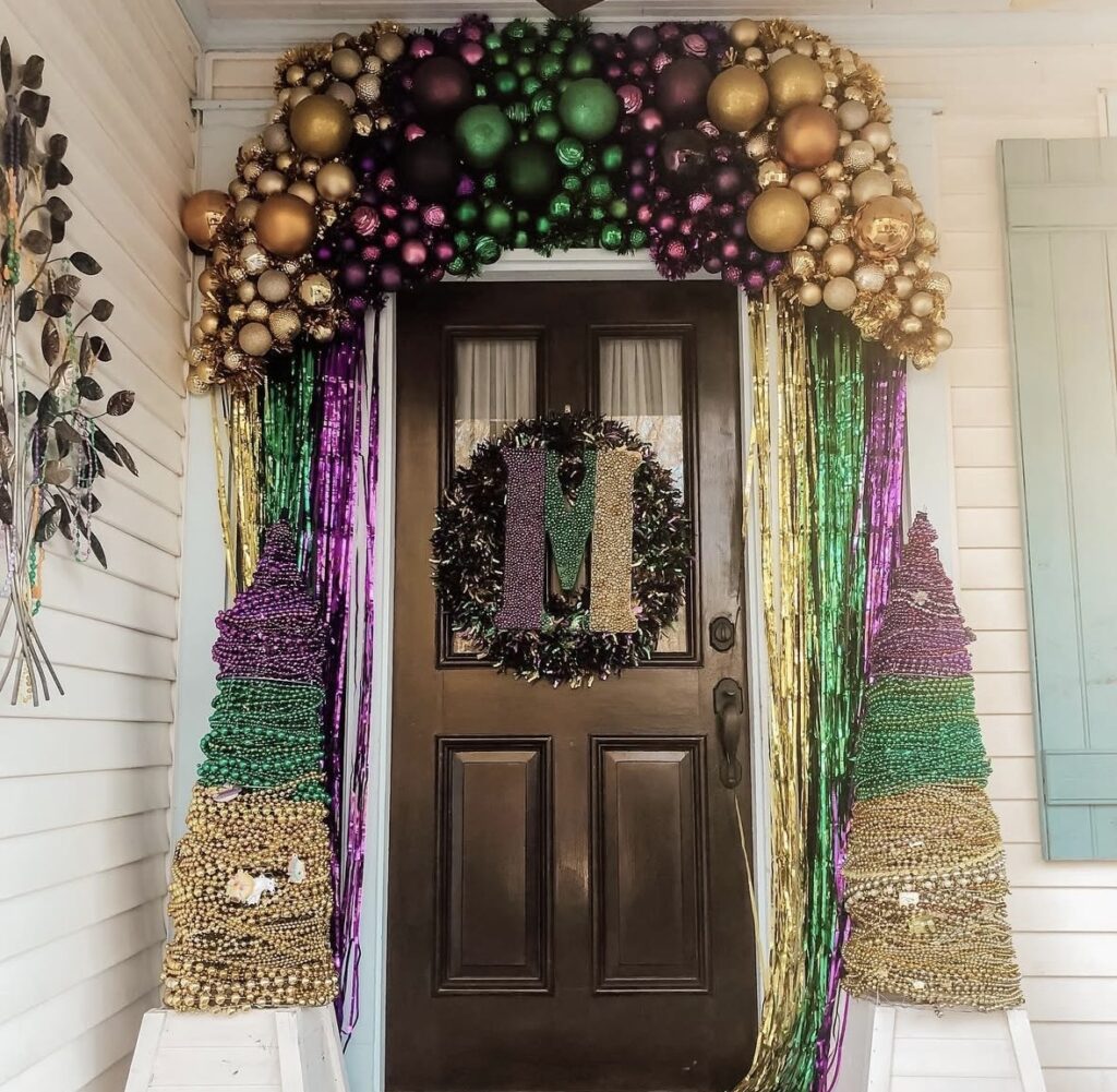 Level 2 Mardi Gras front door decor with a fuller topper, streamers, and stronger purple, green, and gold framing.