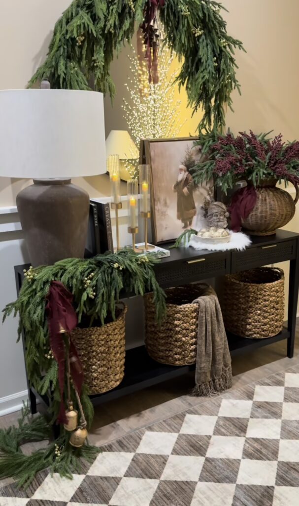 Christmas console table decorated with evergreen garland, baskets, Santa artwork, and cozy neutral holiday accents, featured by slowestuff.com.