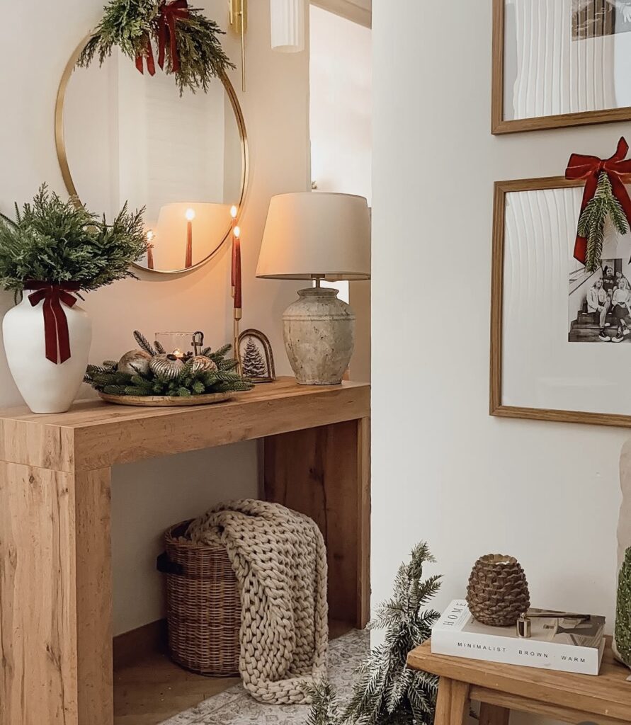 Neutral Christmas console table decorated with a round mirror, evergreen greenery, candles, and a woven basket, featured by slowestuff.com.