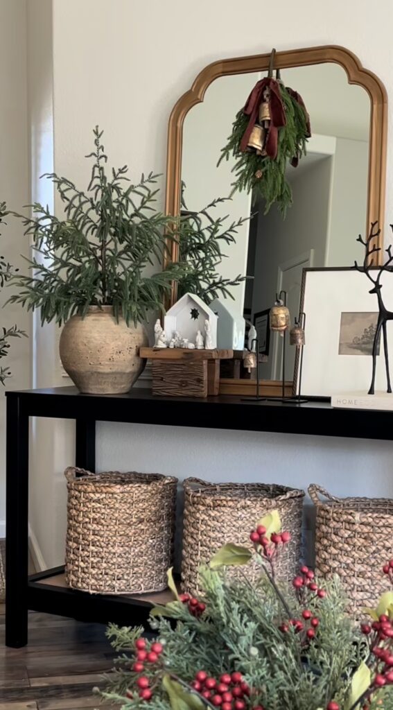 Neutral Christmas entryway console table styled with a nativity scene, bells, greenery, baskets, and natural holiday decor, featured by slowestuff.com.