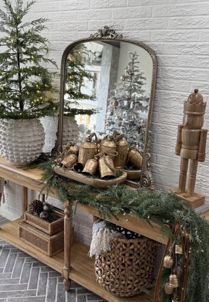 Christmas entryway table decorated with bells, a dough bowl, small potted Christmas trees, and a nutcracker, featured by slowestuff.com.
