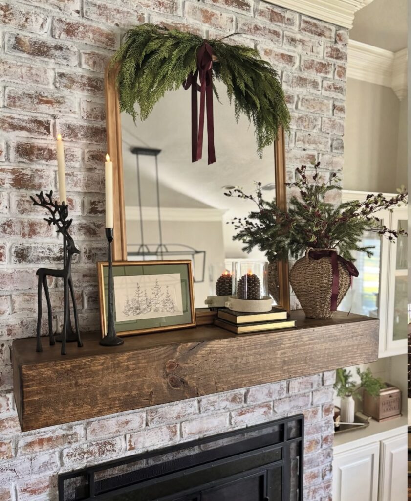 Brick fireplace mantel decorated with lush Christmas greenery and burgundy ribbon for a simple traditional holiday look, featured by slowestuff.com.