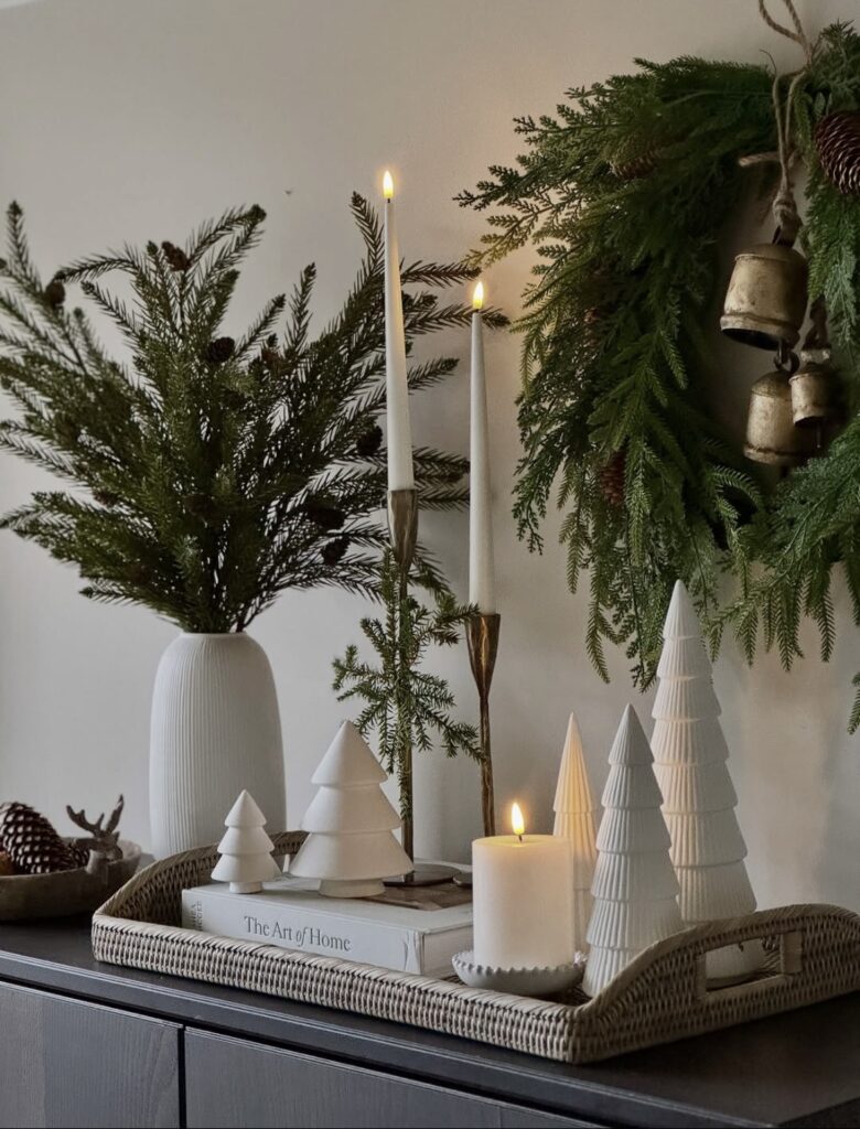 Christmas mantel decorated with a woven tray, white Christmas trees, greenery, a wreath, and decorative bells, featured by slowestuff.com.