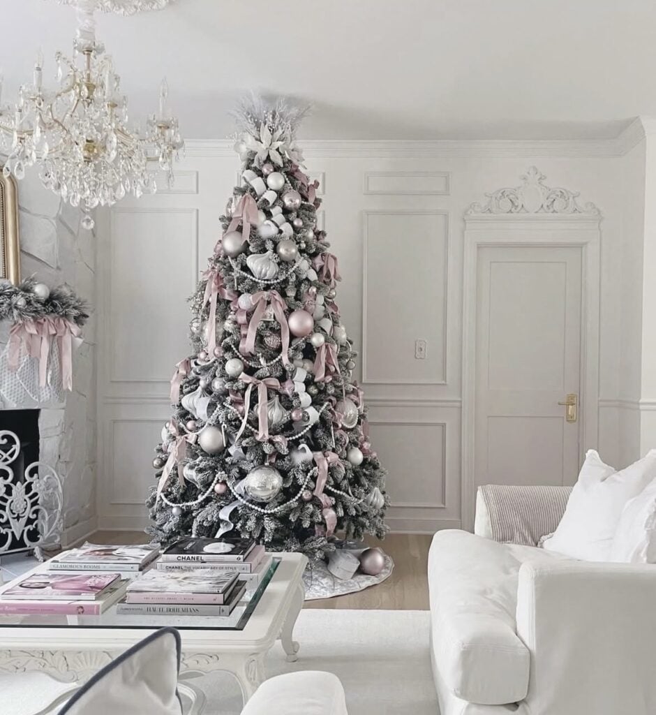 Flocked Christmas tree decorated with blush pink bows, pearl garlands, silver ornaments, and soft pink accents in an elegant white living room.