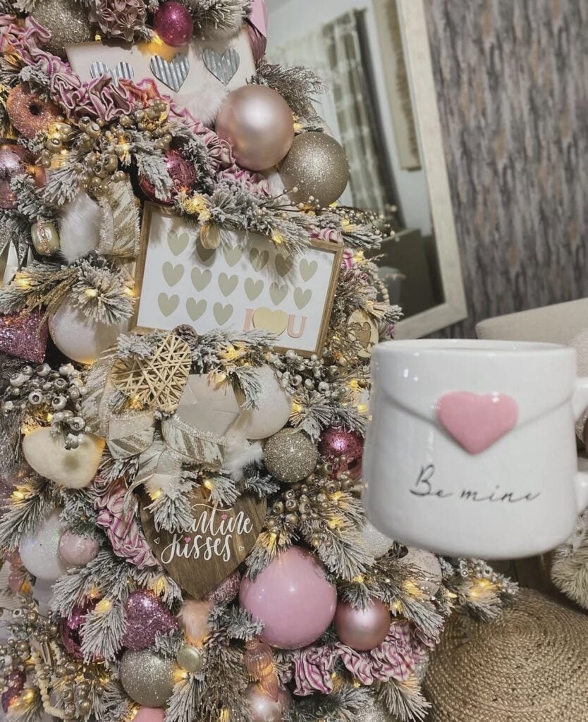 Flocked Valentine tree decorated with blush, champagne, and pink ornaments, heart accents, a “Valentine kisses” sign, and a “Be mine” mug in the foreground.