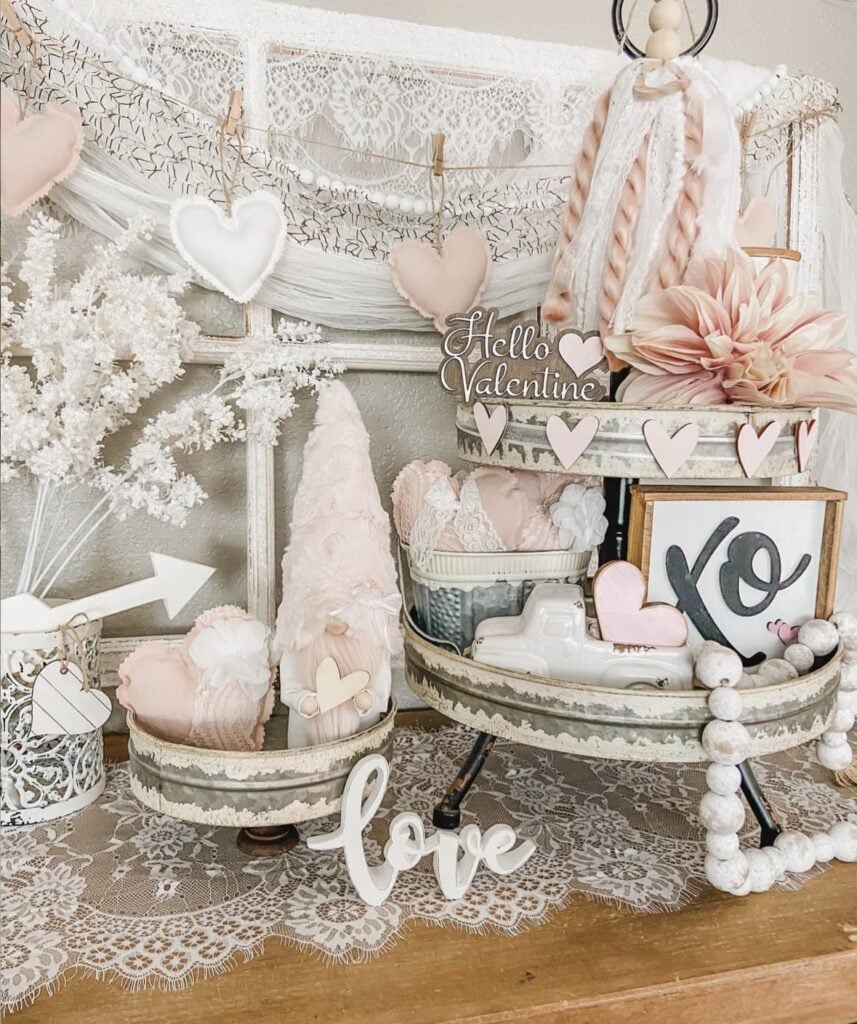 Romantic farmhouse Valentine tiered tray decor with lace, heart garland, “Hello Valentine” sign, gnome accents, “XO” art, and wood bead details.