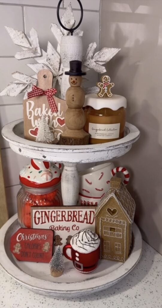 Red and white gingerbread baking tiered tray with mugs, cookie jars, and Christmas signs on a kitchen counter.