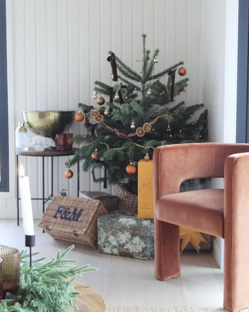 Small cute Yule tree decorated with natural ornaments, pinecones, greenery, orange garland and soft seasonal lighting.