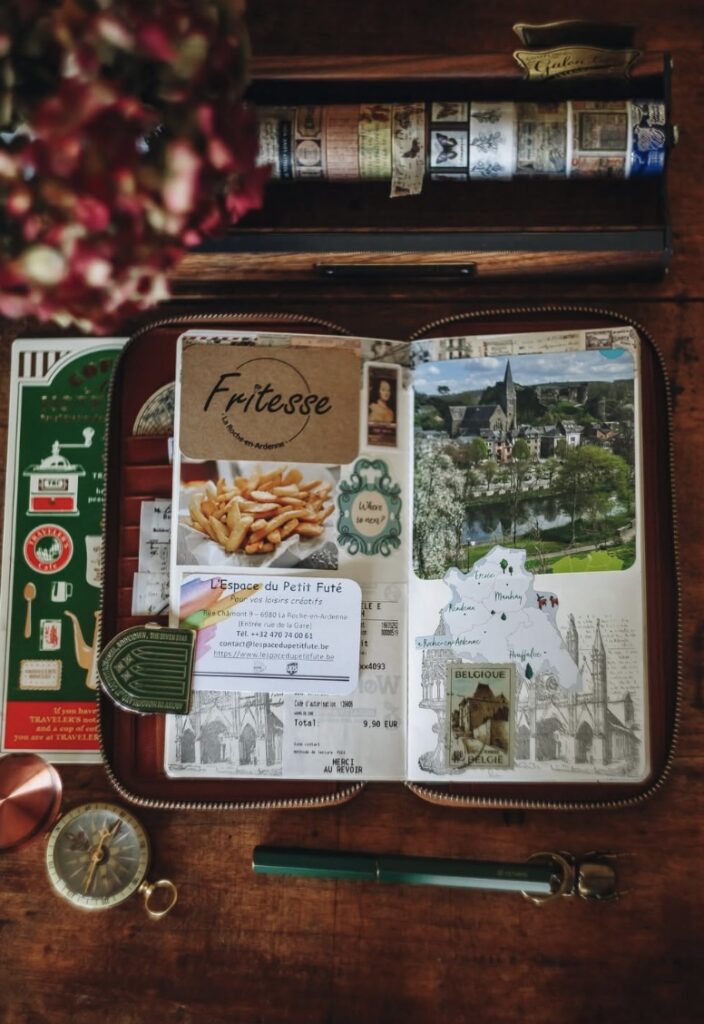 Cozy flat lay of an open travel journal spread titled “Fritesse” with food photo, receipt ephemera, and a Belgium map illustration, surrounded by washi tape and travel tools