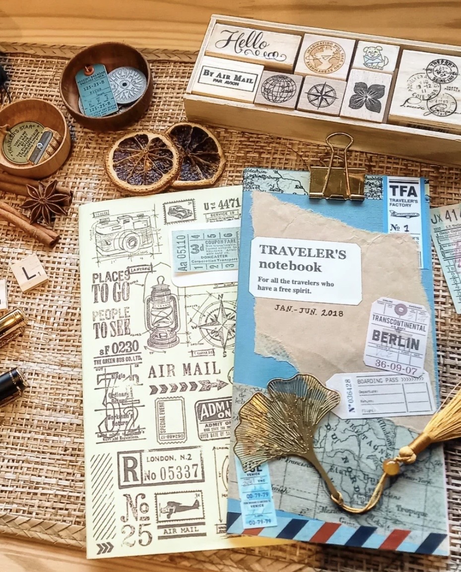 Travelers notebook with stamps of travel images and sayings, with a blue book and clip