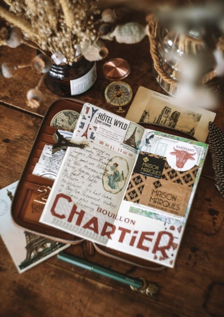 Warm-toned travel journal spread titled “CHARTIER” with layered ephemera, handwritten journaling, and vintage-style labels, photographed on a desk with compass, dried flowers, and stationery.
