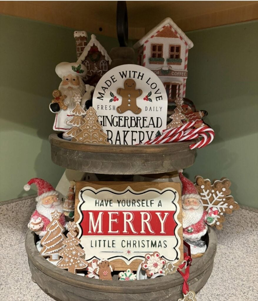 White gingerbread bakery tiered tray styled with gingerbread houses, mini signs, mugs, and Christmas cookies on a kitchen counter.