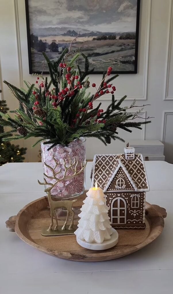 Gingerbread house centerpiece on a tray with peppermint candy vase, reindeer figurine, and frosted Christmas trees.