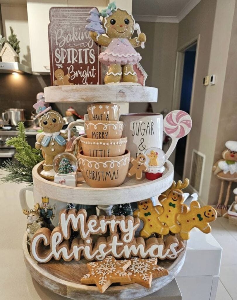 Gingerbread baking spirit tiered tray with mugs, cookie jars, and gingerbread signs on a festive kitchen counter.
