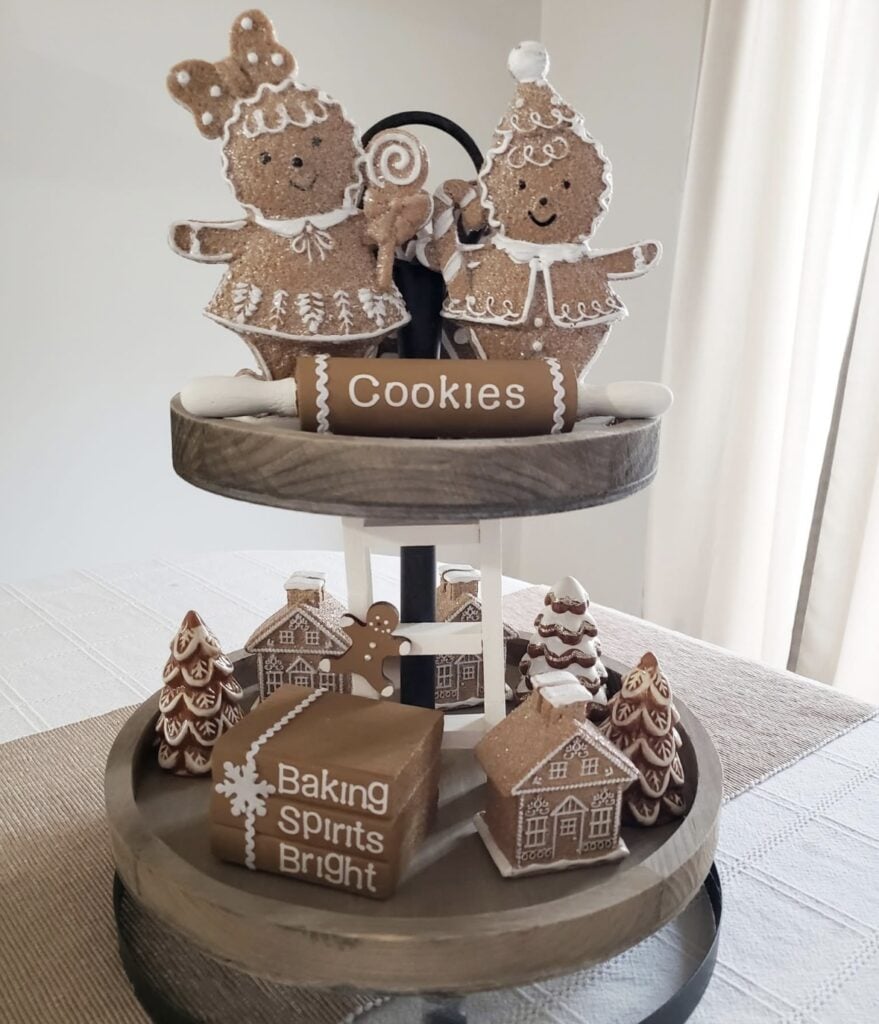 Two tier gingerbread tray filled with cookie ornaments, gingerbread houses, and candy accents styled for Christmas.