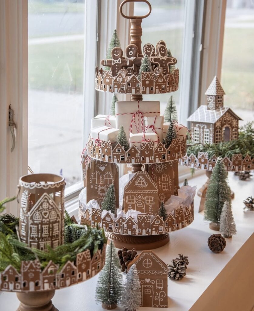 Tiered tray styled as a gingerbread village with houses and bottle brush trees displayed in front of a frosty window.
