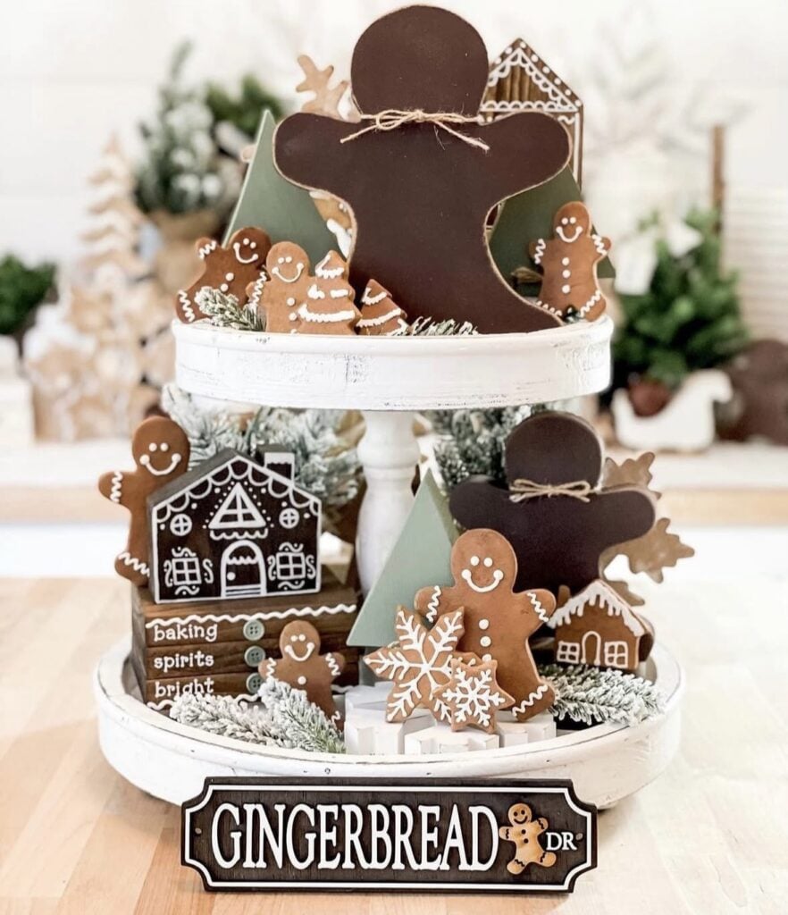 White tiered tray filled with gingerbread cookie decor, gingerbread street sign, and candy accents for Christmas.
