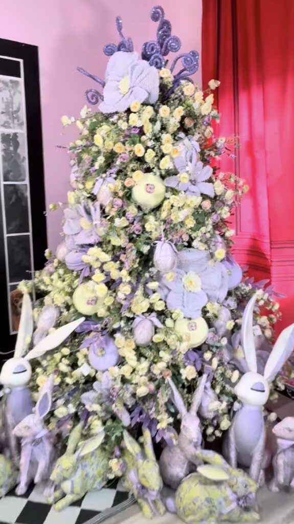 Whimsical lavender and green Easter tree decorated with soft flowers, large pastel eggs, and white bunny figurines around the base.