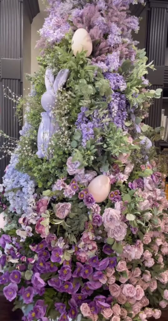 Floral Easter tree covered in purple and pink spring flowers with greenery, large decorative eggs, and a bunny silhouette tucked into the branches.