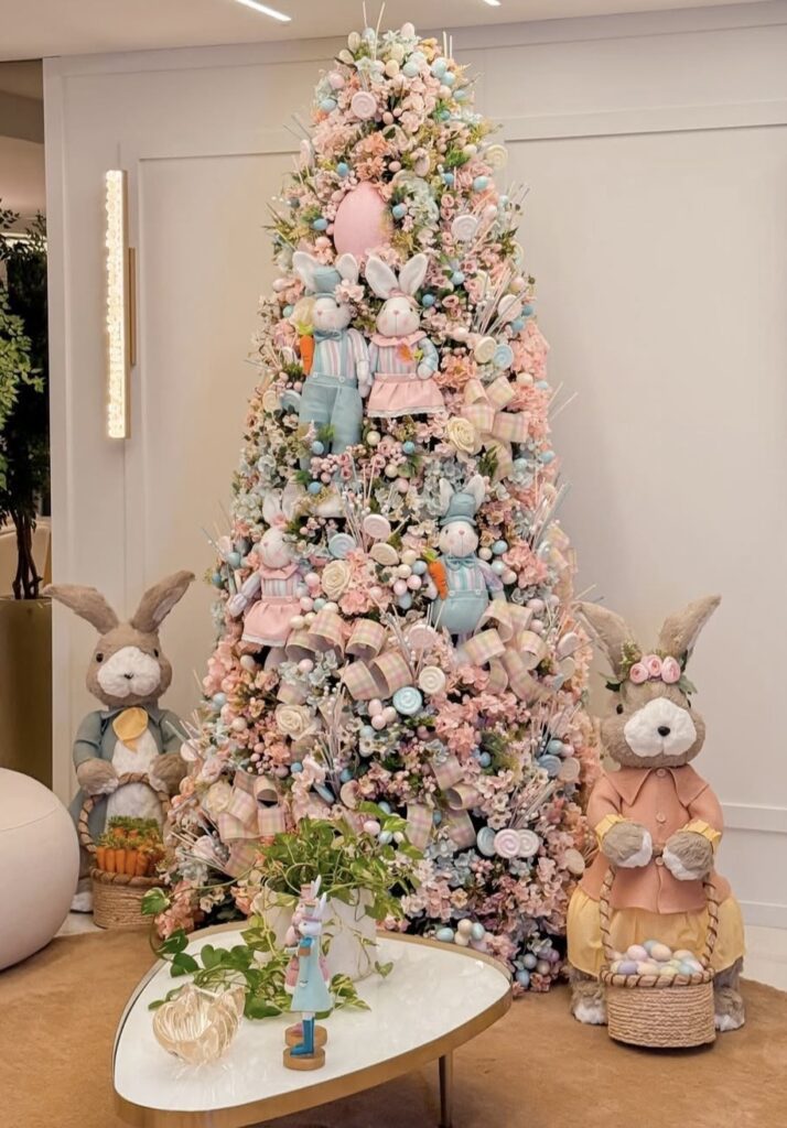 Pink pastel Easter tree filled with ribbons, flowers, bunny plush ornaments, and large rabbit figures standing beside the tree with Easter baskets.