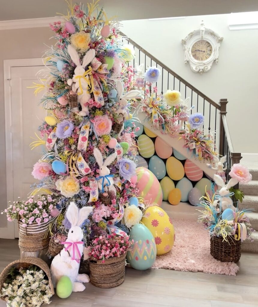 Colorful Easter tree covered in spring florals, pastel eggs, and bunny accents with oversized Easter eggs on a staircase backdrop.