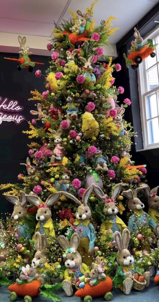 Tall Easter Christmas tree filled with bunny figurines, bright pink flowers, and carrot decorations with large rabbits displayed at the base.