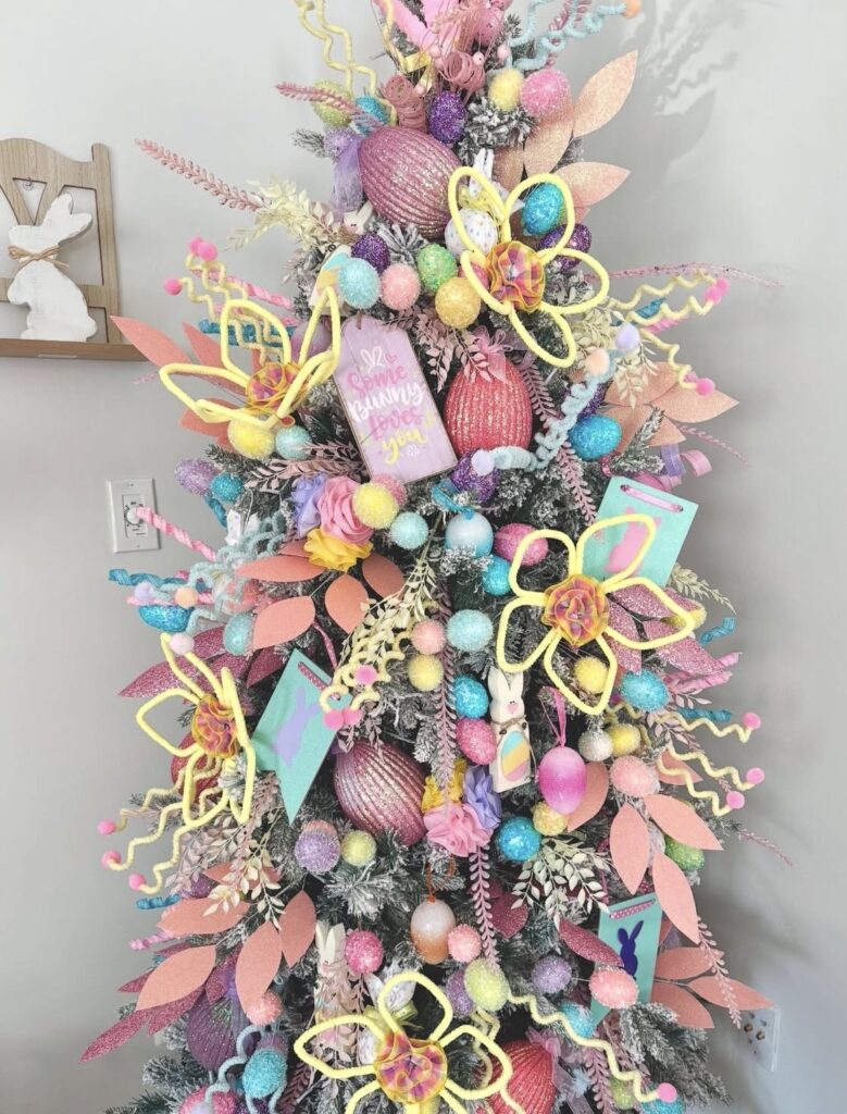 Colorful Easter tree with pastel pom pom garland, glitter eggs, bright spring flowers, and a “Some Bunny Loves You” sign