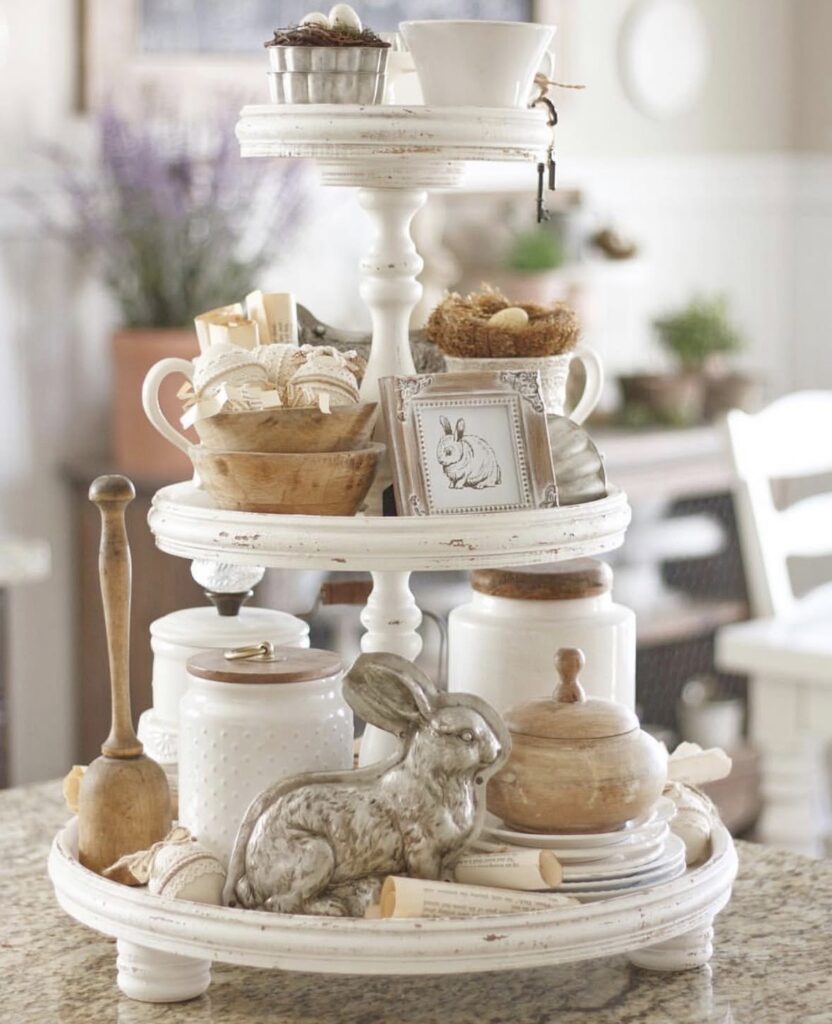 Farmhouse Easter tiered tray featuring white dishes, wooden bowls, bunny artwork, and neutral spring decor with a rustic kitchen aesthetic.