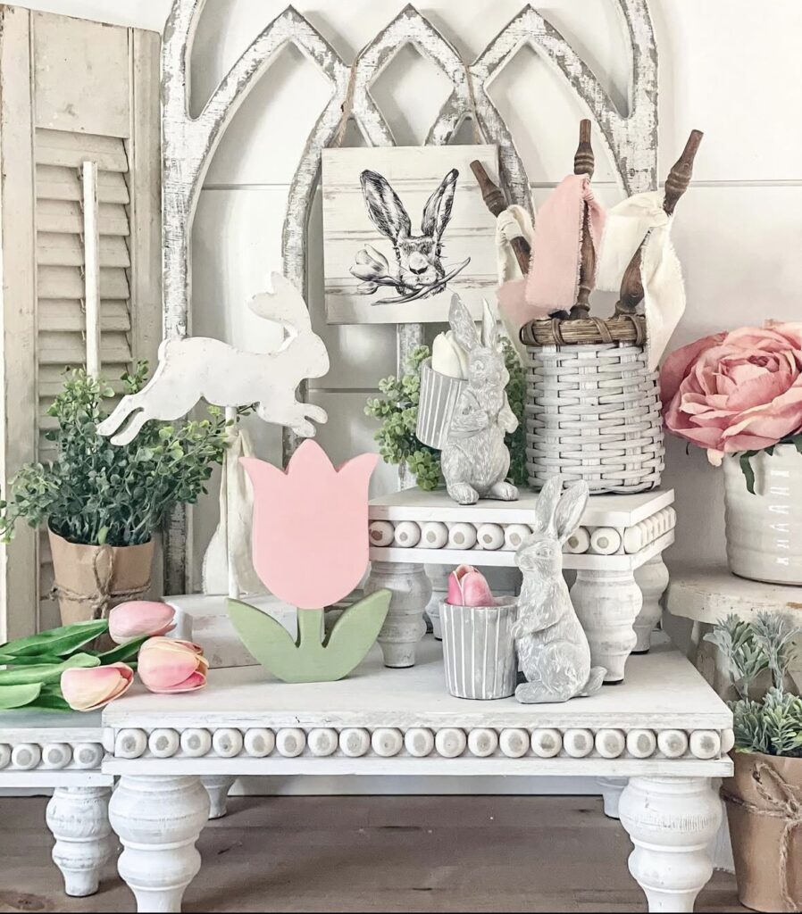 Neutral Easter tiered tray decor with white risers, pink tulip accents, bunny figurines, and vintage farmhouse styling in soft spring colors.