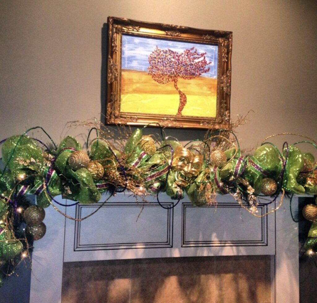 Mardi Gras mantel garland with green glitter ribbon, gold ornaments, and a gold carnival mask above a fireplace.