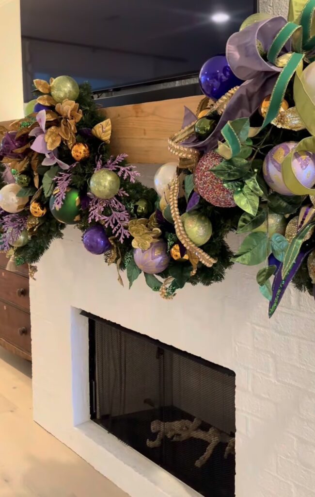 Close up of a white fireplace with an ornate garland decorated with large balls in traditional mardi gras colors