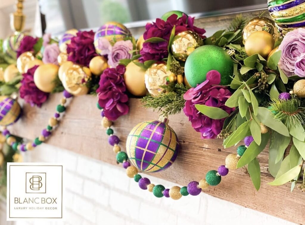 Close-up of a Mardi Gras floral mantel garland with purple flowers, greenery, gold ornaments, a purple-green-gold plaid bauble, and bead garland.