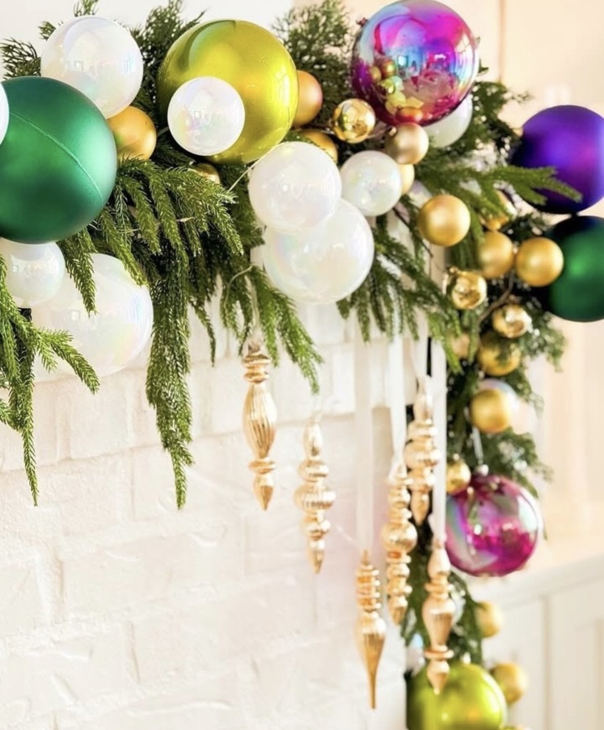 Close-up of Mardi Gras garland detail with evergreen branches, oversized green and purple ornaments, white and gold ornaments, and dangling gold finial ornaments.