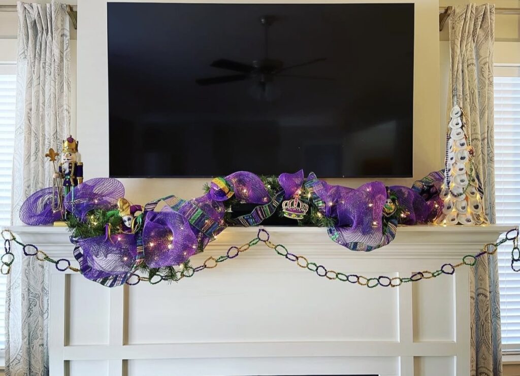 White mantel under a TV with purple mesh ribbon garland, string lights, and a draped Mardi Gras bead chain.