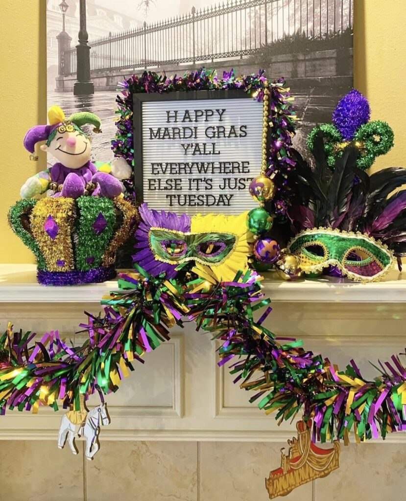 Mardi Gras mantel vignette with masks, tinsel, and a letter board that reads “Happy Mardi Gras y’all… it’s just Tuesday.”