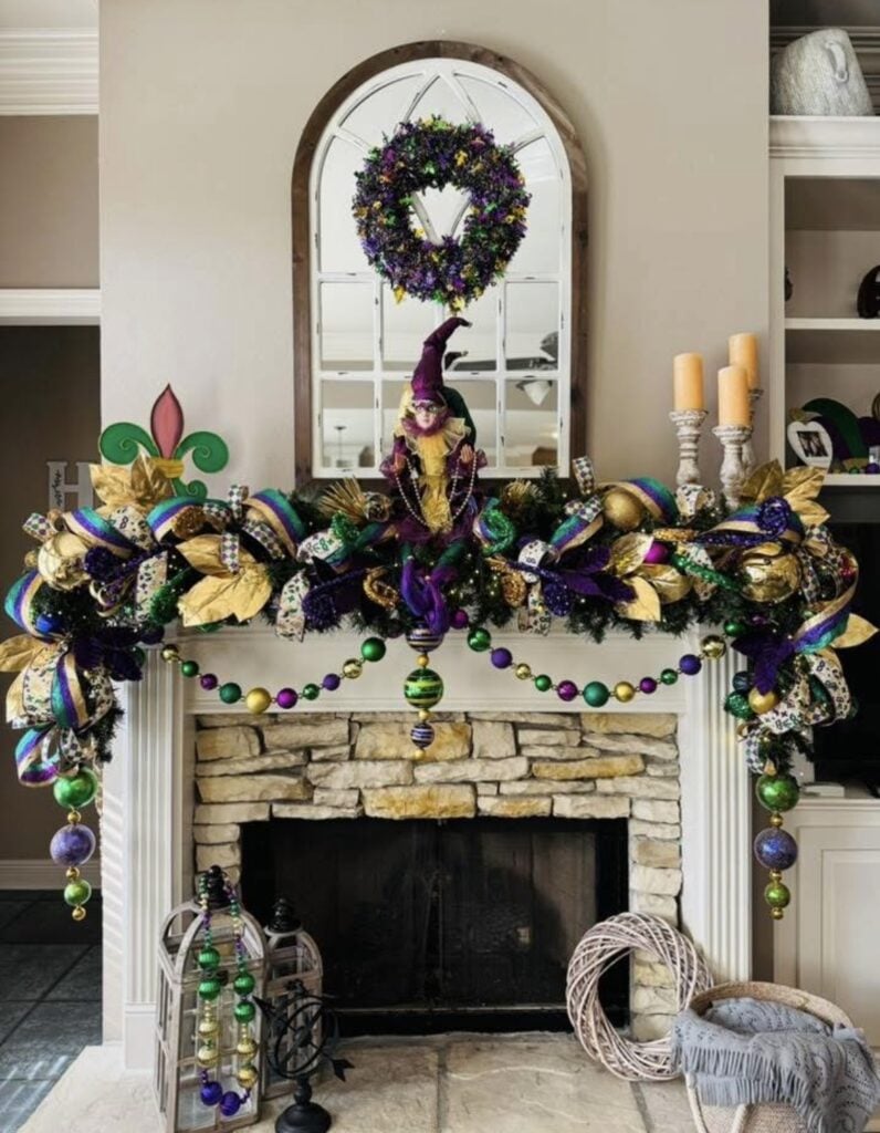 Stone fireplace mantel packed with Mardi Gras ribbon garland, a jester figure, and bead garlands in purple, green, and gold.