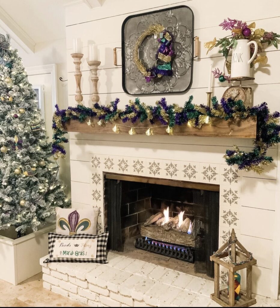 Farmhouse style fireplace with a lit Mardi Gras tinsel garland, fleur de lis pillow, and a Christmas tree in the background.