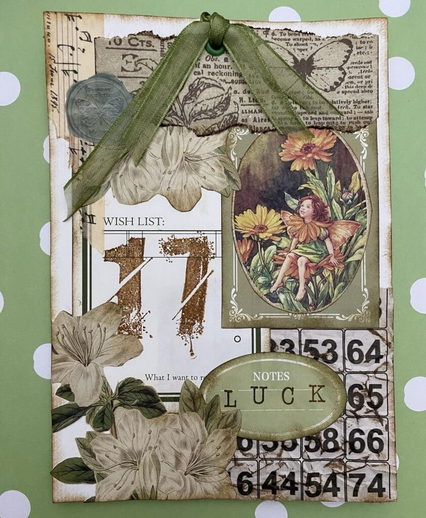 Vintage-style mixed media tag with earthy greens, gold number 17, floral cutouts, and a small fairy illustration layered over old book pages and ephemera.