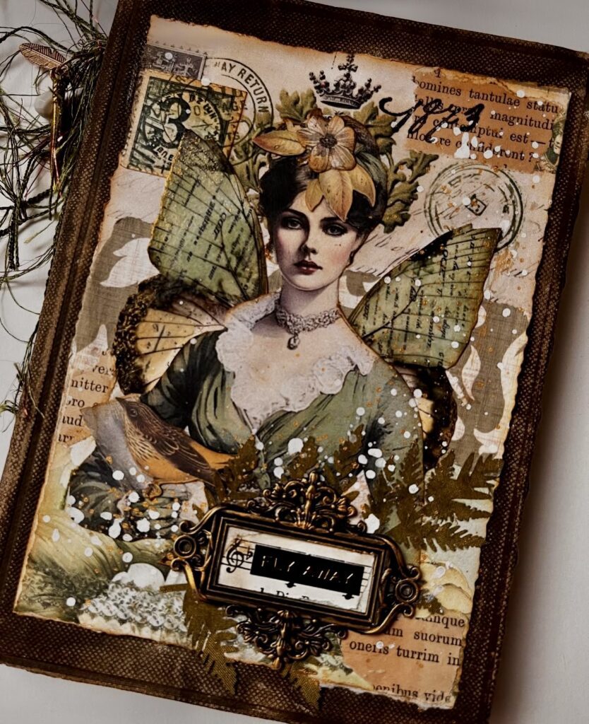 Vintage mixed media journal cover with a Victorian-style fairy woman, green dress and wings, ornate gold frame, and distressed background textures.