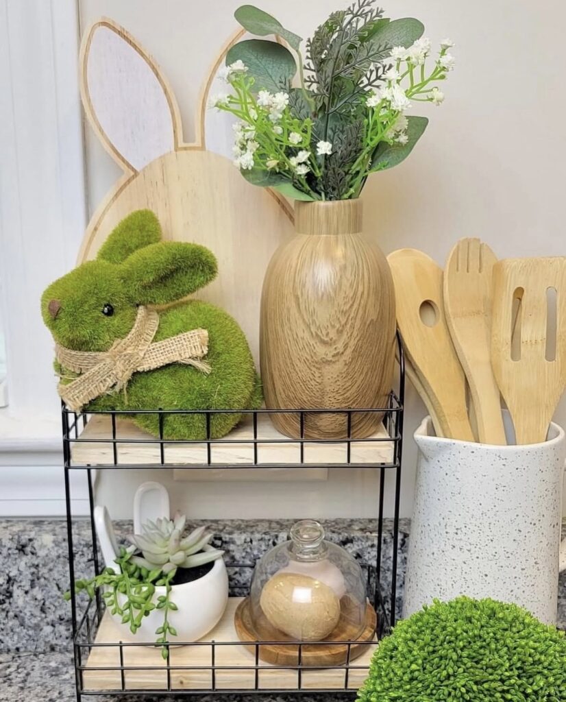 Simple spring kitchen shelf decor with moss bunny, wood vase of greenery, bunny cutting board, small succulents, and neutral accents.