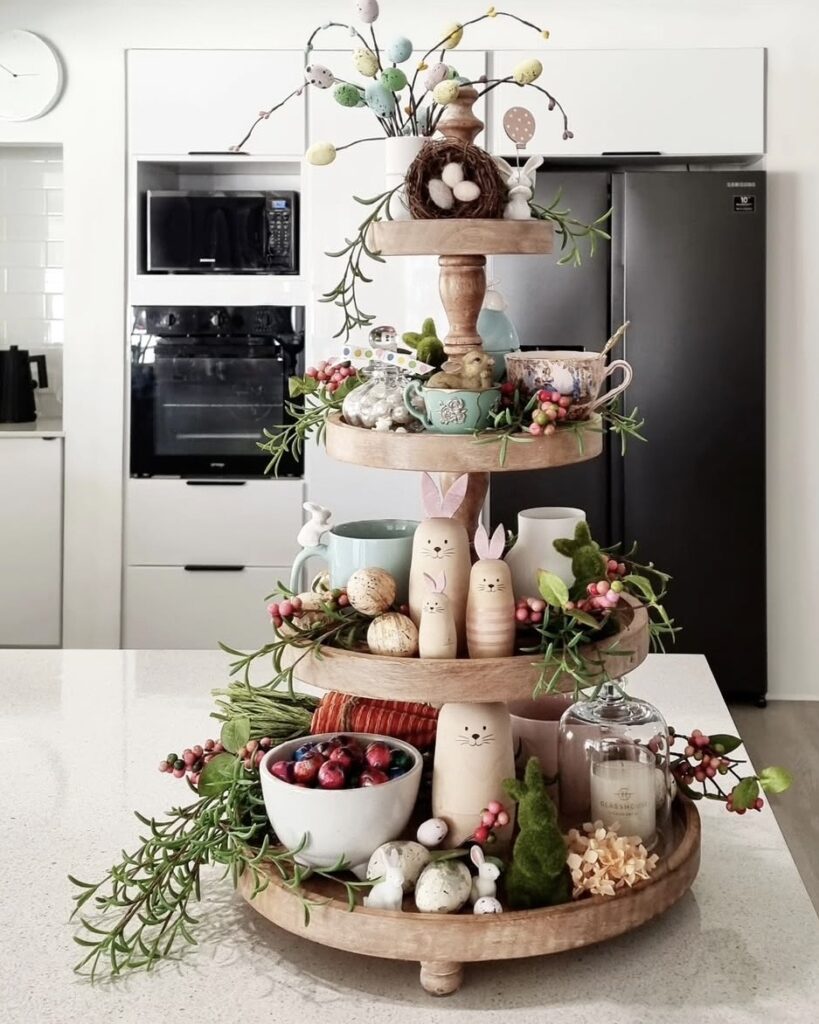 Large Easter tiered tray centerpiece with pastel bunny figures, speckled eggs, greenery garland, berries, a candle cloche, and spring decor.