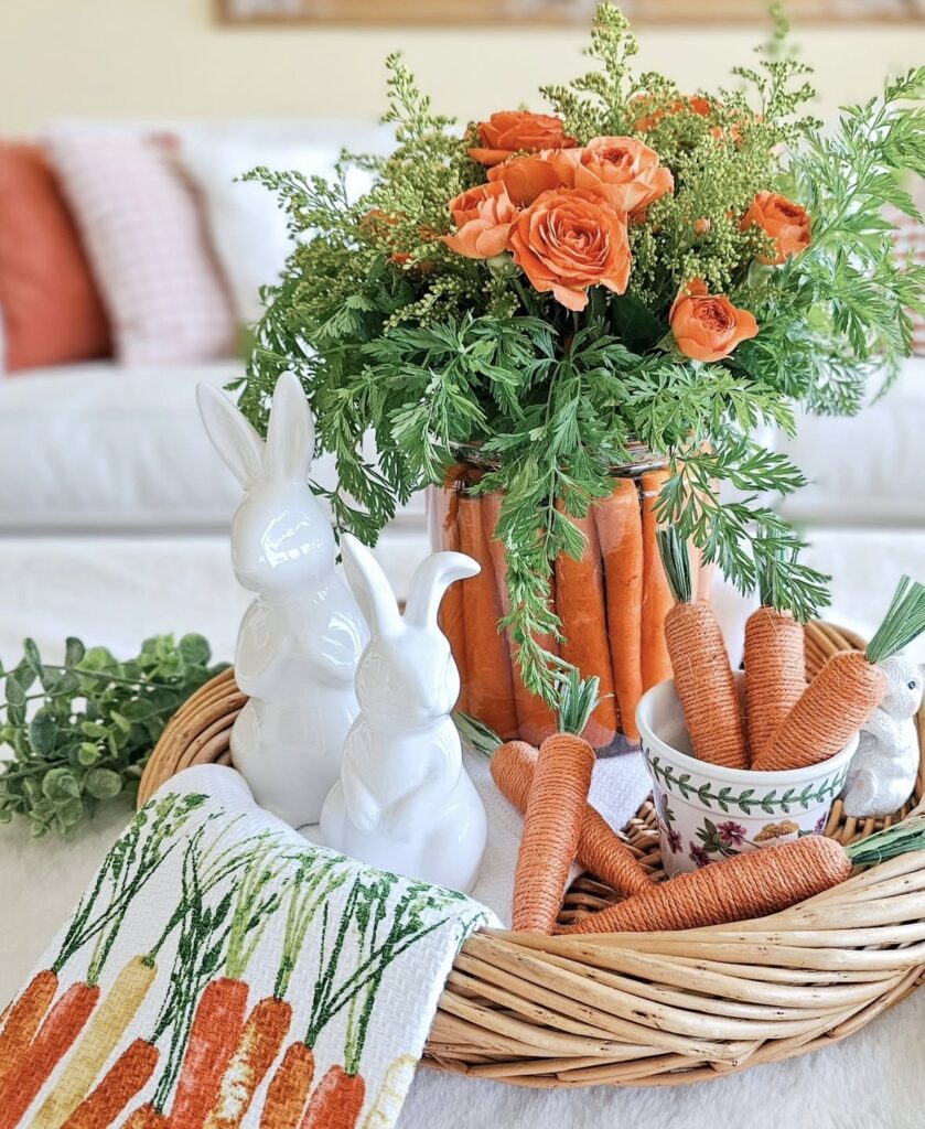 Wicker tray Easter centerpiece with carrot-filled vase, orange roses, white ceramic bunny figurines, and carrot dish towel.