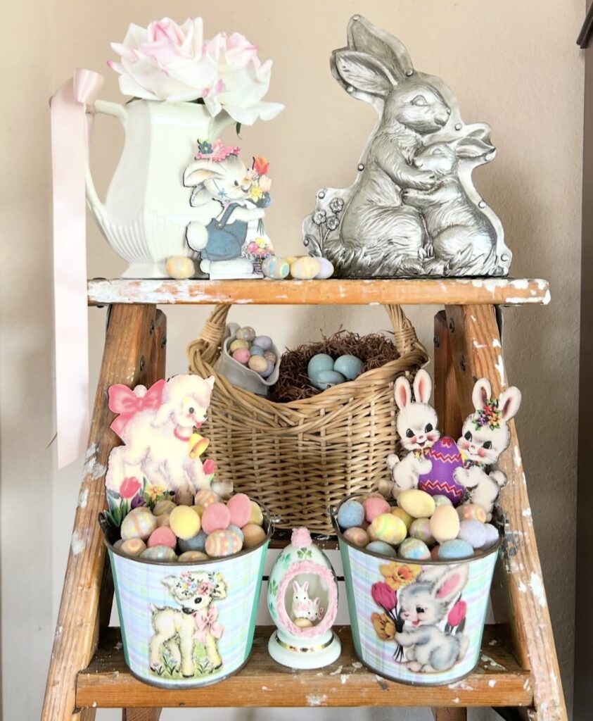 Vintage ladder shelf Easter decor with pastel egg buckets, bunny cutouts, wicker basket, pink ribbon pitcher, and silver bunny plaque.