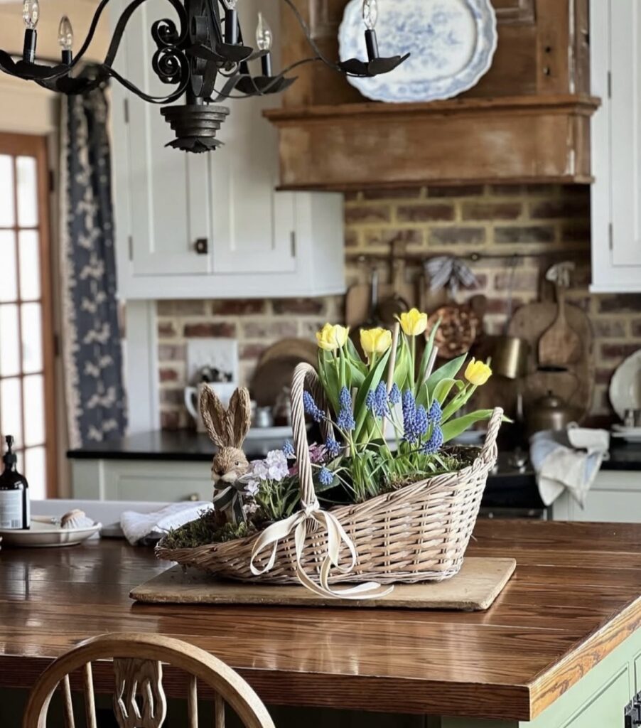 Farmhouse kitchen island spring centerpiece with wicker basket of yellow tulips, blue grape hyacinths, moss, and rustic bunny figurine.